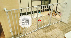 Metallic baby gate on a wooden floor with a visible brand logo.