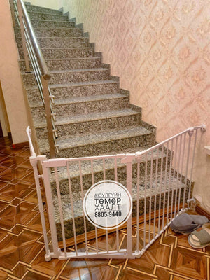 Baby gate in front of a staircase with decorative wallpaper and wooden floor.