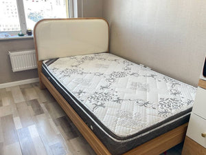 Bed with a mattress in a room with a window and radiator.