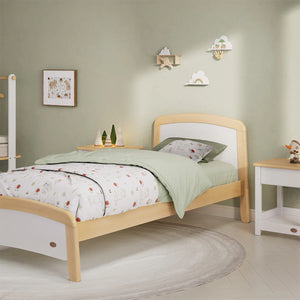 Wooden bed with green bedding in a room with light green walls and white furniture.