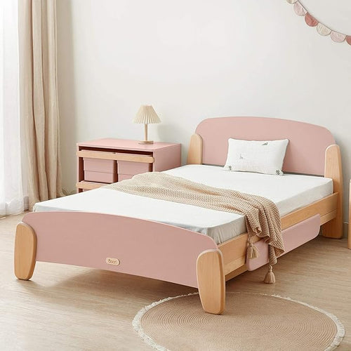 Pink and wooden bed in a room with a lamp and side table.