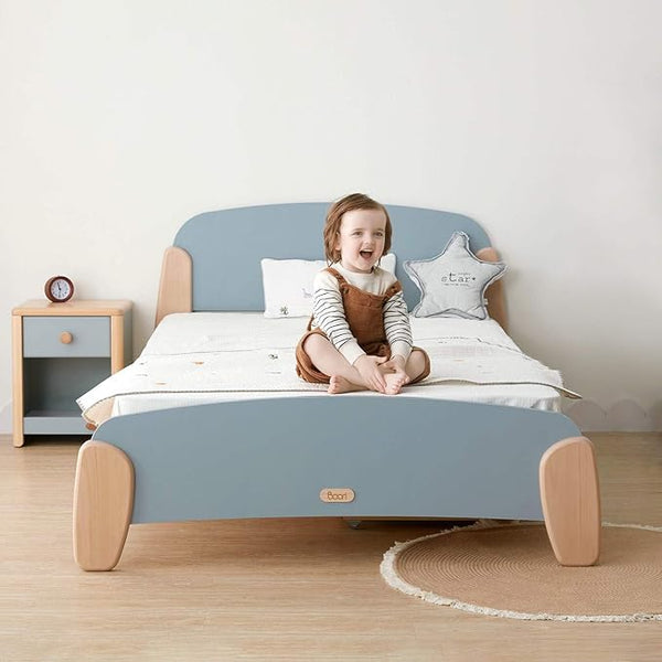 Child sitting on a blue and wooden bed with a nightstand in the background
