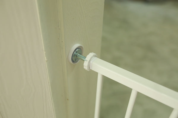 White baby gate attached to a wooden door with a blurred background