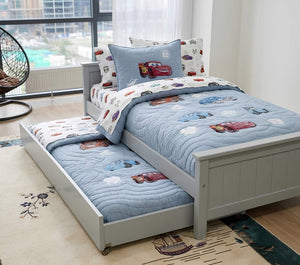Children's bed with blue and white bedding featuring cartoon cars, in a bright room with large windows.