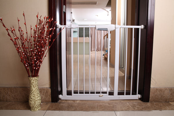 White baby gate installed in a doorway with decorative red branches in a vase on the left.