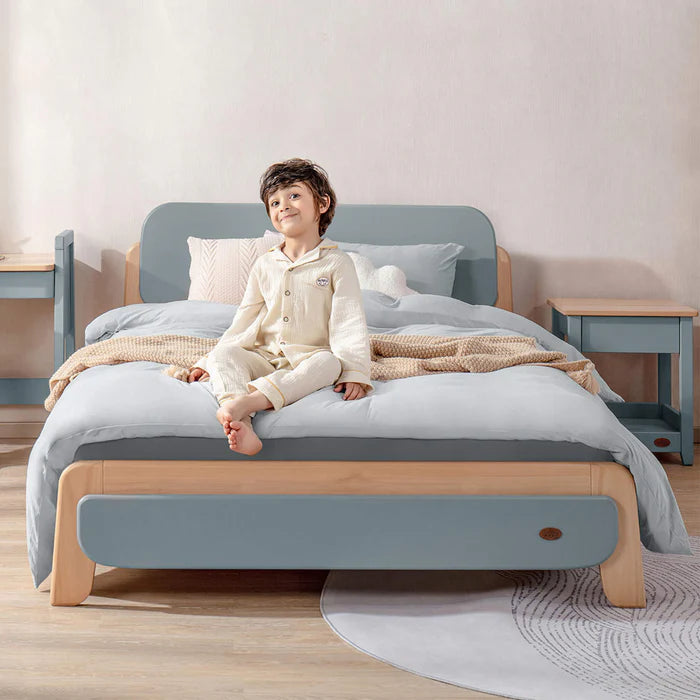 Child sitting on a bed with a light blue and wooden frame in a room.
