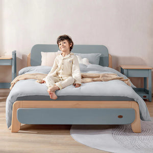 Child sitting on a bed with a light blue and wooden frame in a room.