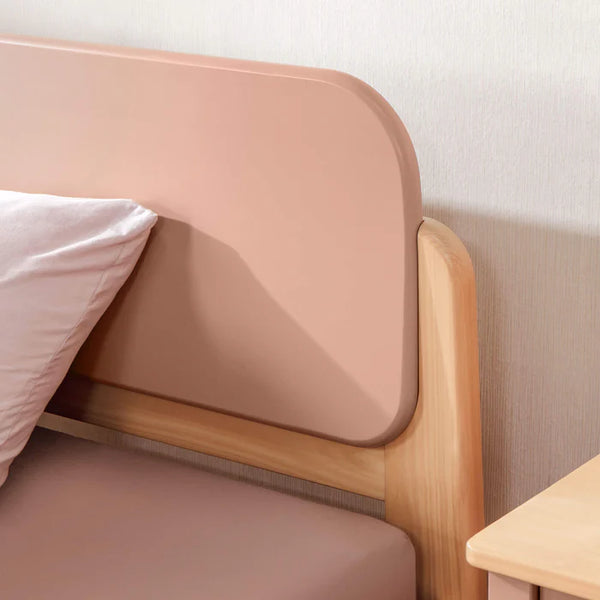 Close-up of a modern bed with wooden frame and pink headboard against a white wall.