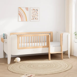 Wooden crib in a room with a round rug and wall art