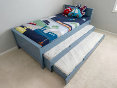 Children's bed with toy cars and planes on a colorful mattress, featuring a pull-out trundle.