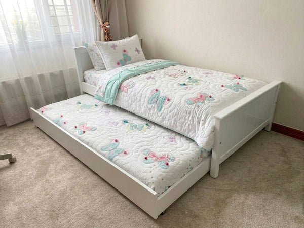 White bed with floral bedding in a room with curtains and a radiator.