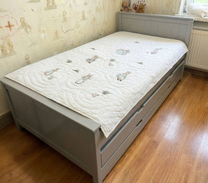 Gray bed with a white mattress featuring cartoon designs on a wooden floor.