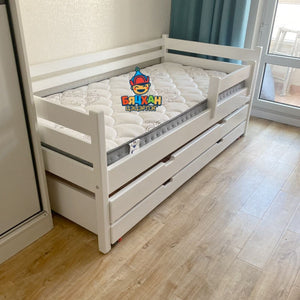 White children's bed with drawers on a wooden floor, featuring a visible brand logo.