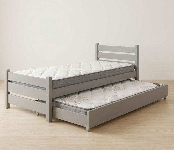 Gray bed frame with a mattress and pull-out trundle on a wooden floor.