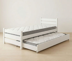 White bed frame with a mattress and pull-out trundle on a wooden floor.