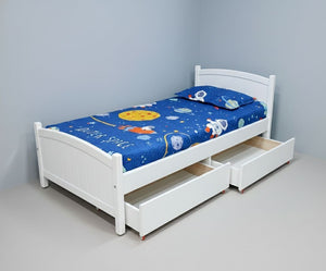 White bed with blue space-themed mattress and white drawers against a gray wall.