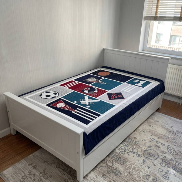 Bed with a sports-themed bedspread in a room with a window and radiator.