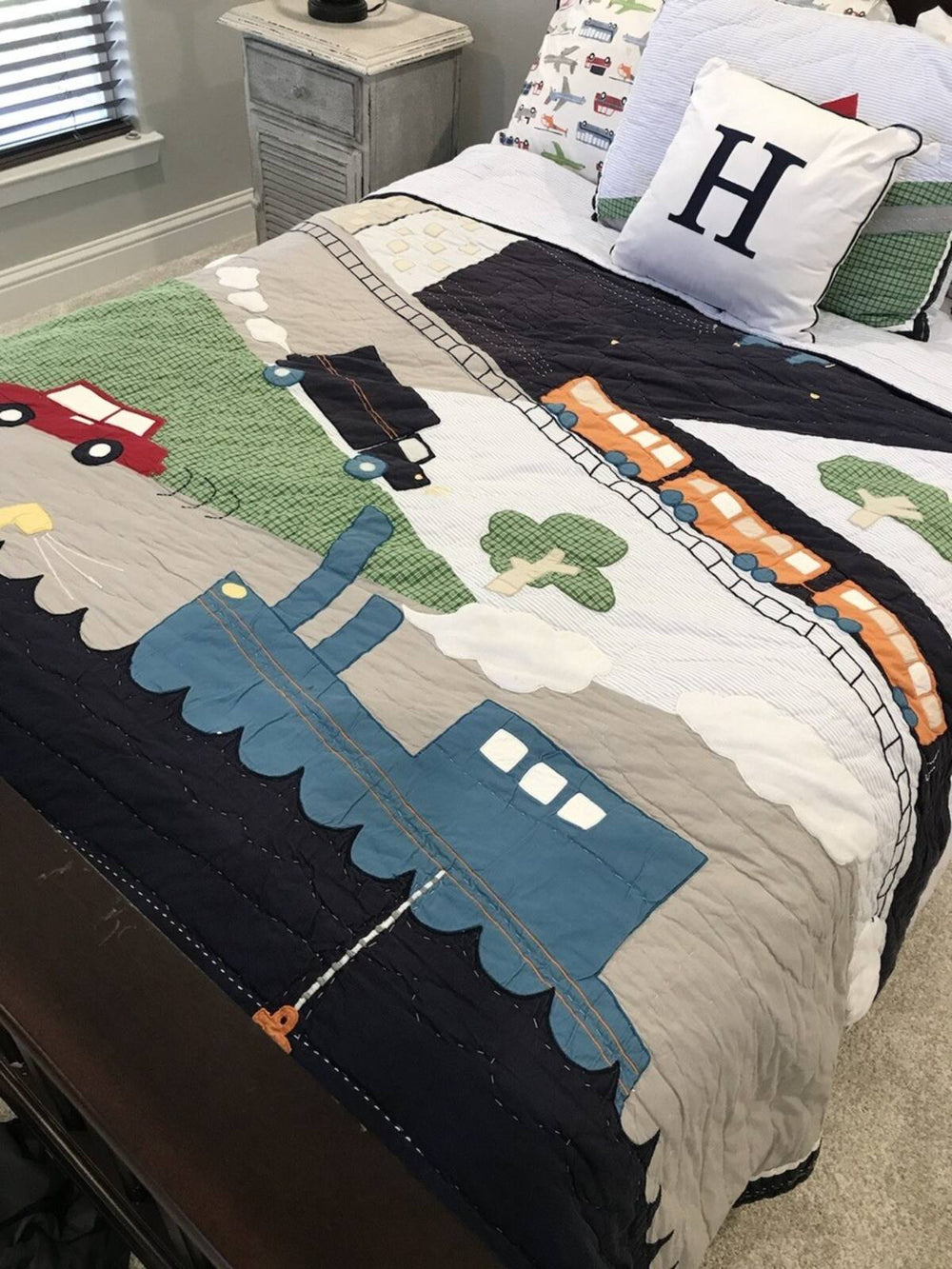Children's bedspread with train and car design on a bed in a bedroom.