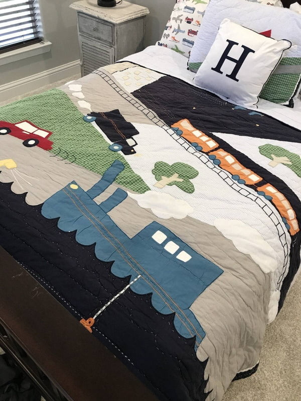 Children's bedspread with train and car design on a bed in a bedroom.