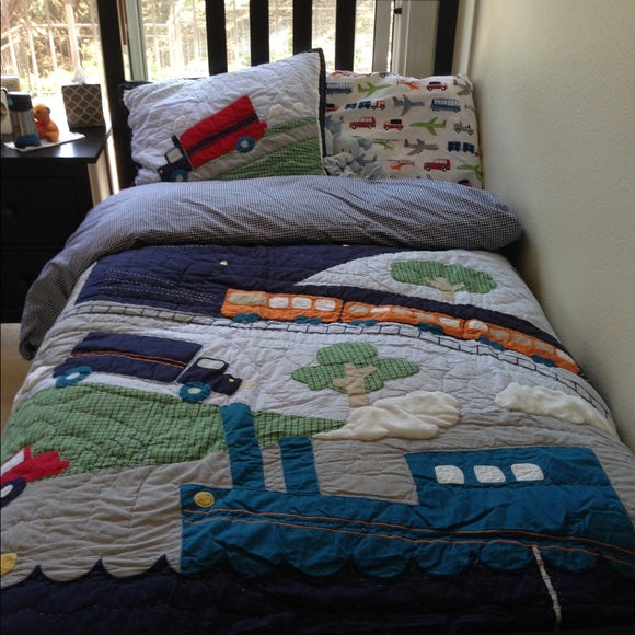 Children's bedspread with train and car design on a bed in a bedroom.