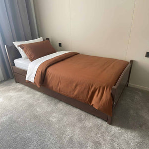 Bed with brown bedding and white pillows in a room with gray carpet and light-colored walls.