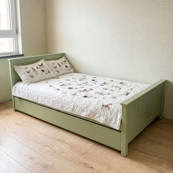 Green bed with white bedding and animal-patterned pillows in a room with a window.
