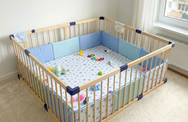 Wooden crib with blue and green bedding and toys on a light-colored floor.
