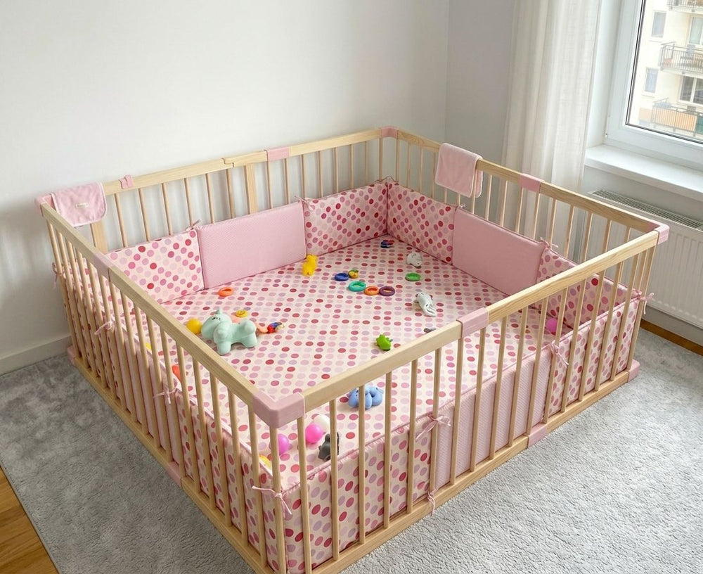 Wooden crib with pink bedding and toys in a room with a window.