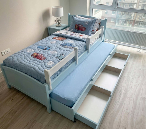 Children's bed with a pull-out trundle in a room with a lamp and window.