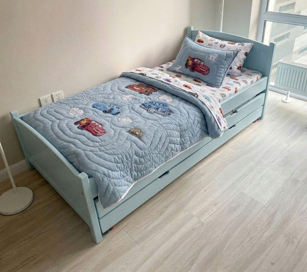 Children's bed with blue bedding and car-themed pillows in a room.
