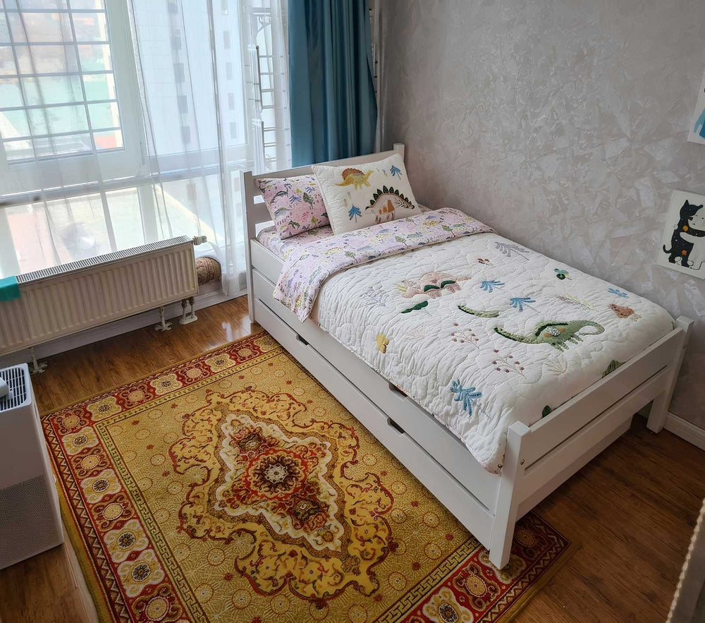 Children's bedroom with a bed featuring a dinosaur-themed quilt and pillows.