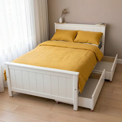 White bed with yellow bedding in a room with light wood flooring and white curtains.