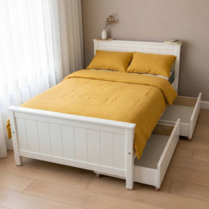 White bed with yellow bedding in a room with light wood flooring and white curtains.