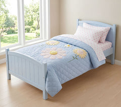 Children's bed with a blue floral quilt in a bright room with large windows.