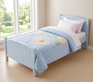 Children's bed with a blue floral quilt in a bright room with large windows.