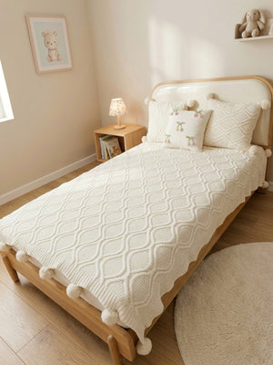 Bedroom with a wooden bed and white textured blanket, side table with lamp, and decor items.